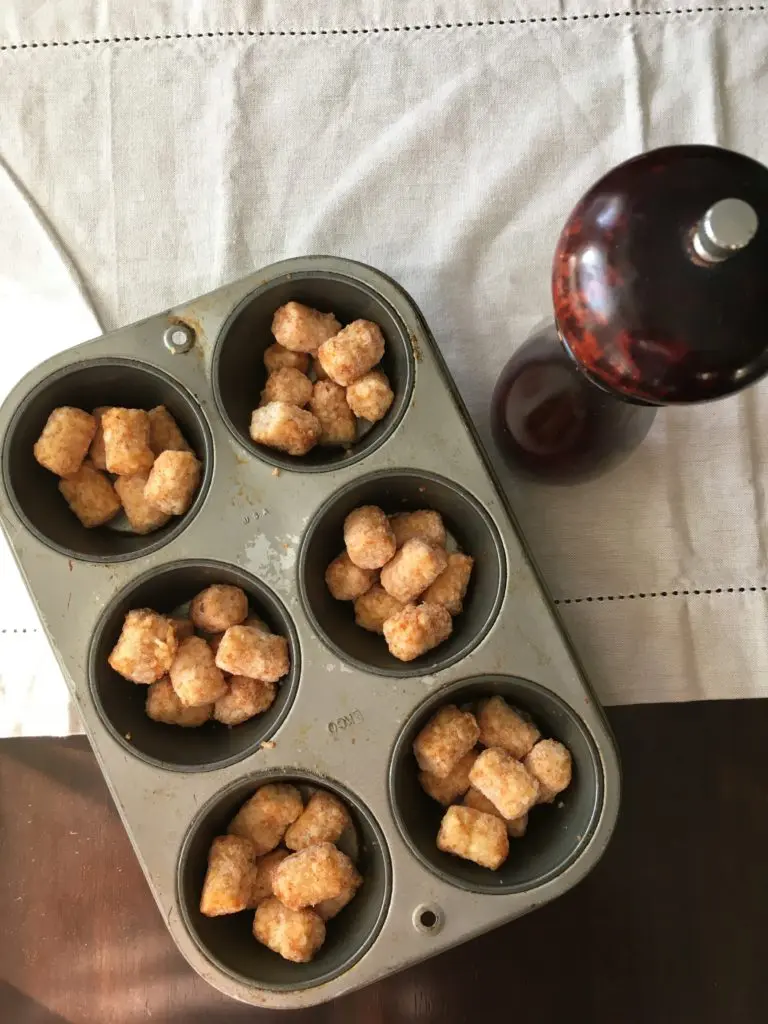 a muffin pan with frozen tater tots in the wells