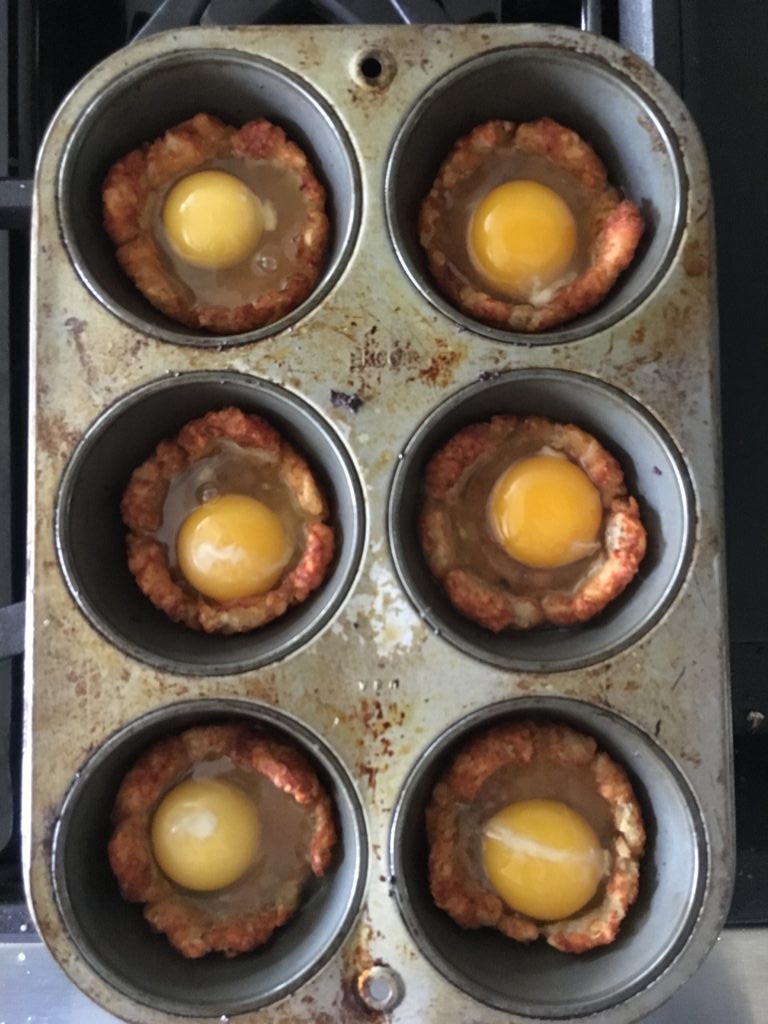cupcake pan with tater tot nests with raw eggs inside, ready for baking