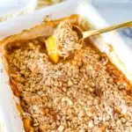 peach crisp in a casserole dish with a golden spoon scooping it.