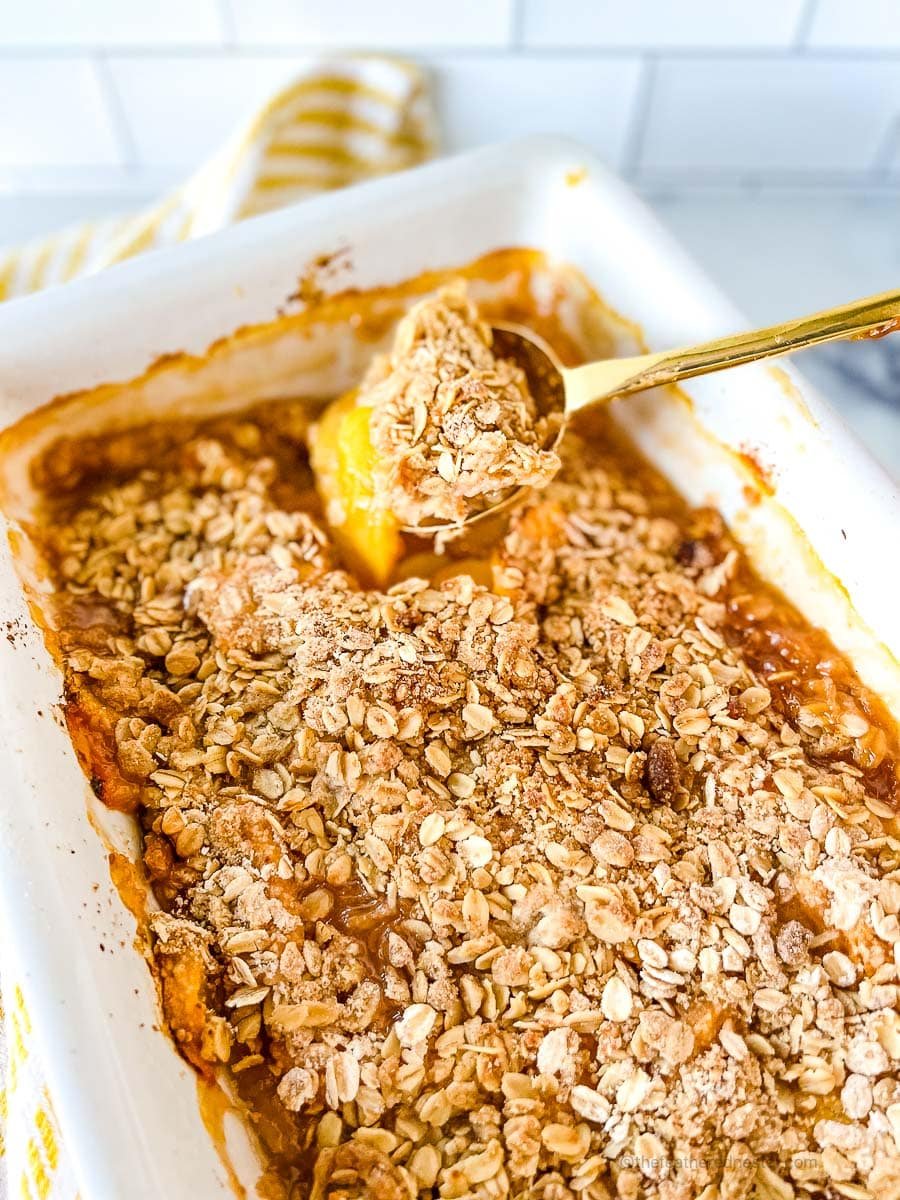 peach crisp in a casserole dish with a golden spoon scooping it.