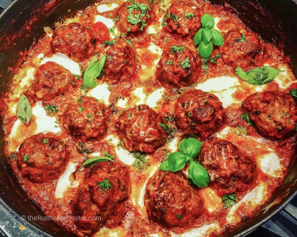 pork and beef meatballs in a skillet with red sauce and melted cheese.