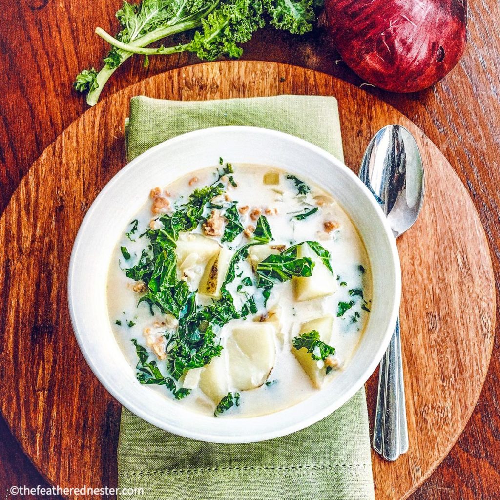 a white bowl of Zuppa Toscana, with spoon and green napkin