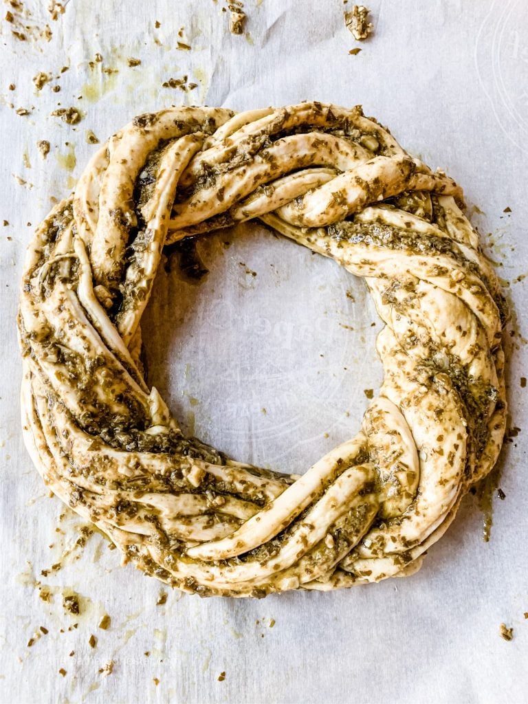 Pesto bread wreath on parchment paper, ready for baking.