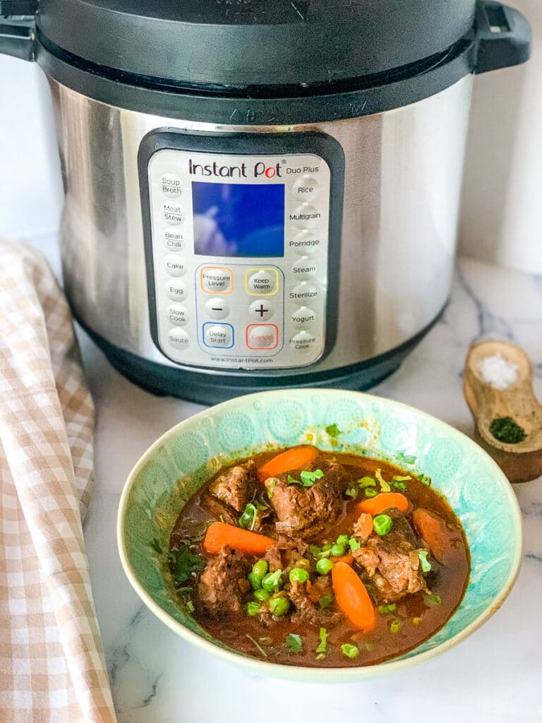 a green bowl of beef stew and an Instant Pot beside it.