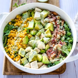 A white bowl of green goddess cobb salad on top of a wooden serving tray.