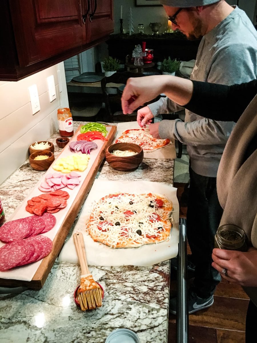 people preparing pizzas on a counter.