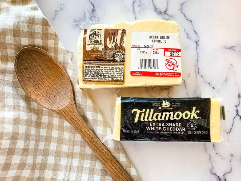 Two blocks of white cheddar cheese on a brown gingham checked cloth napkin.