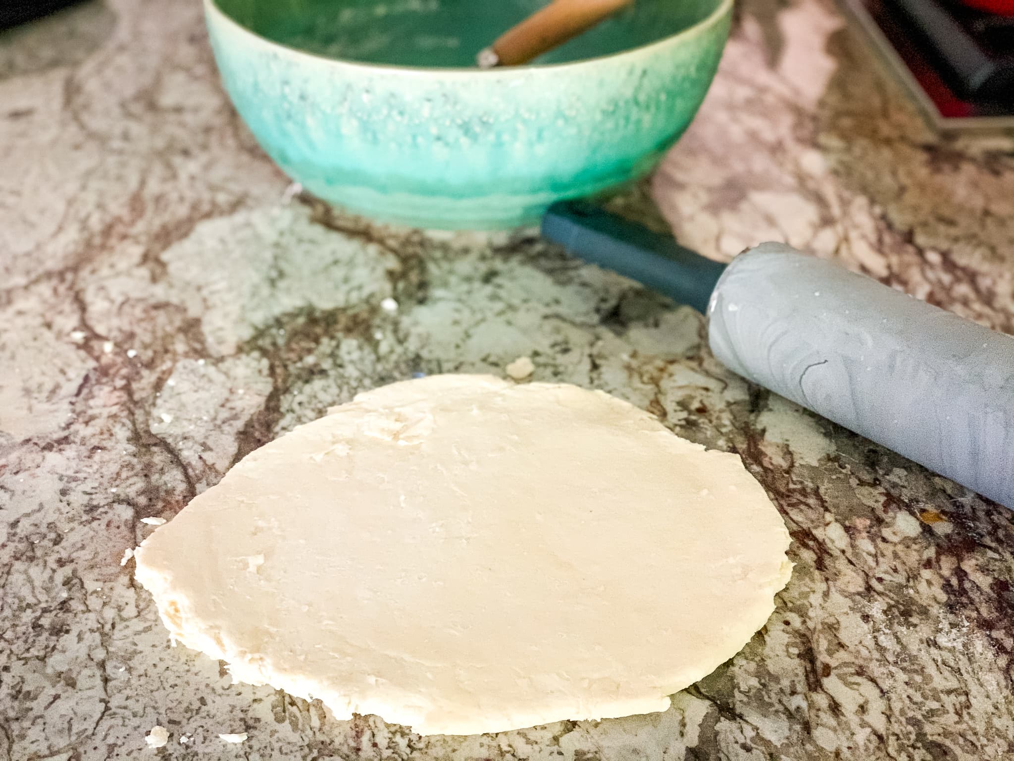 Circle of pastry dough next to a rolling pin on marble counter top.