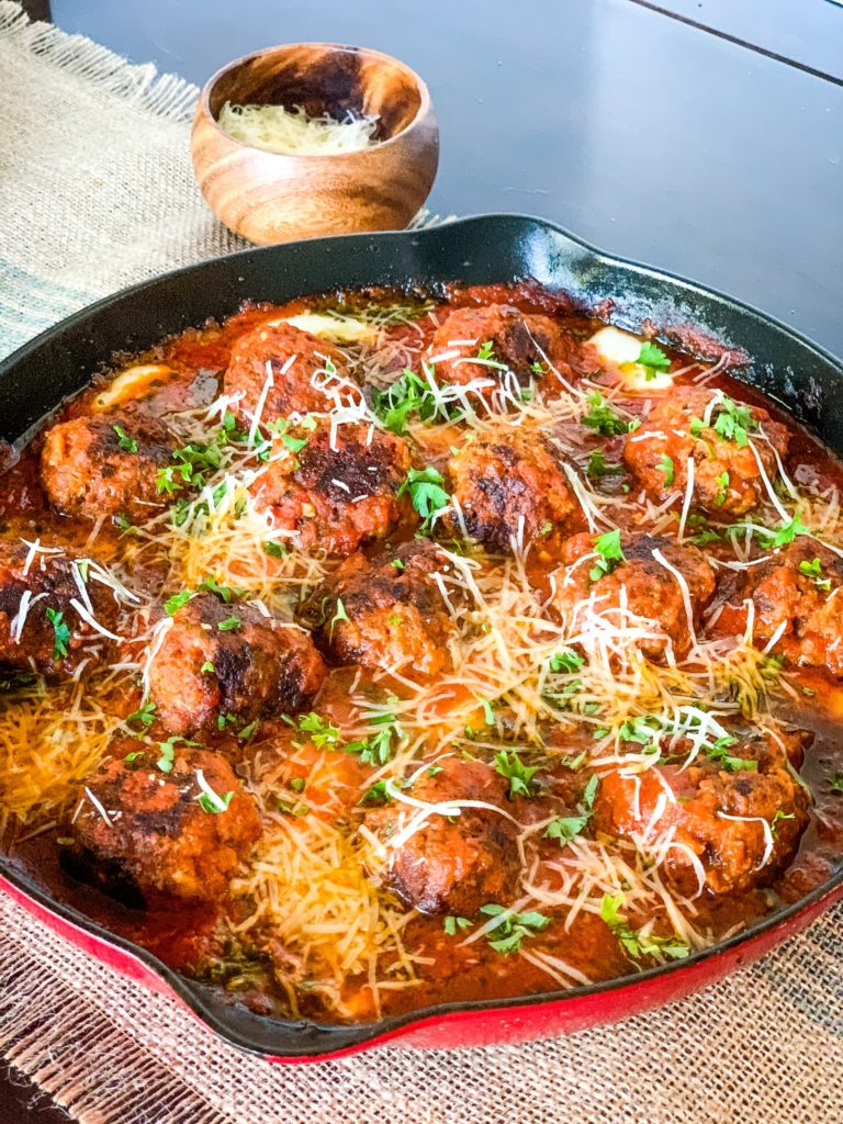 a skillet with marinara meatballs with shredded cheese on top.