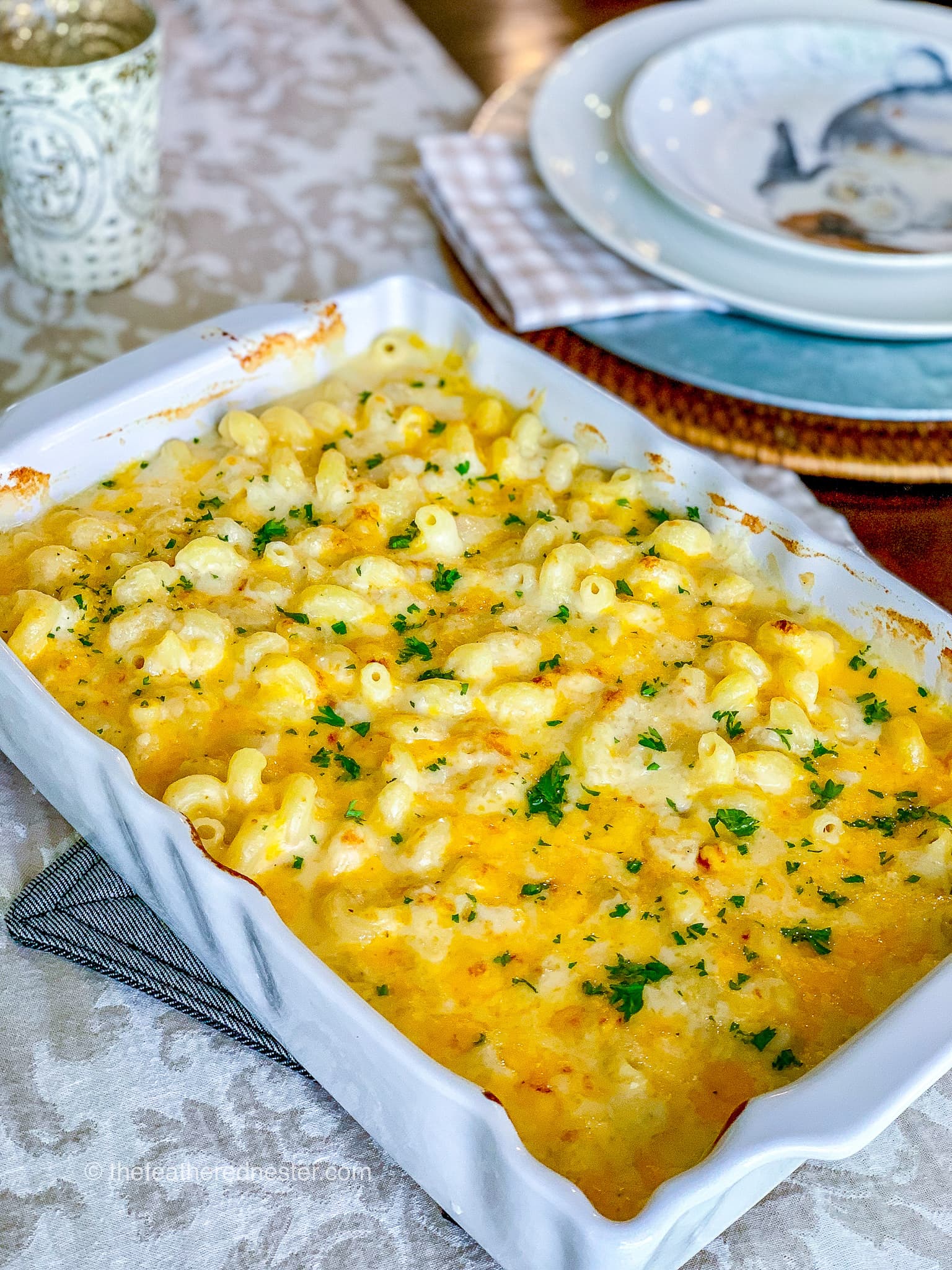A casserole dish of macaroni and cheese with plates in the background.