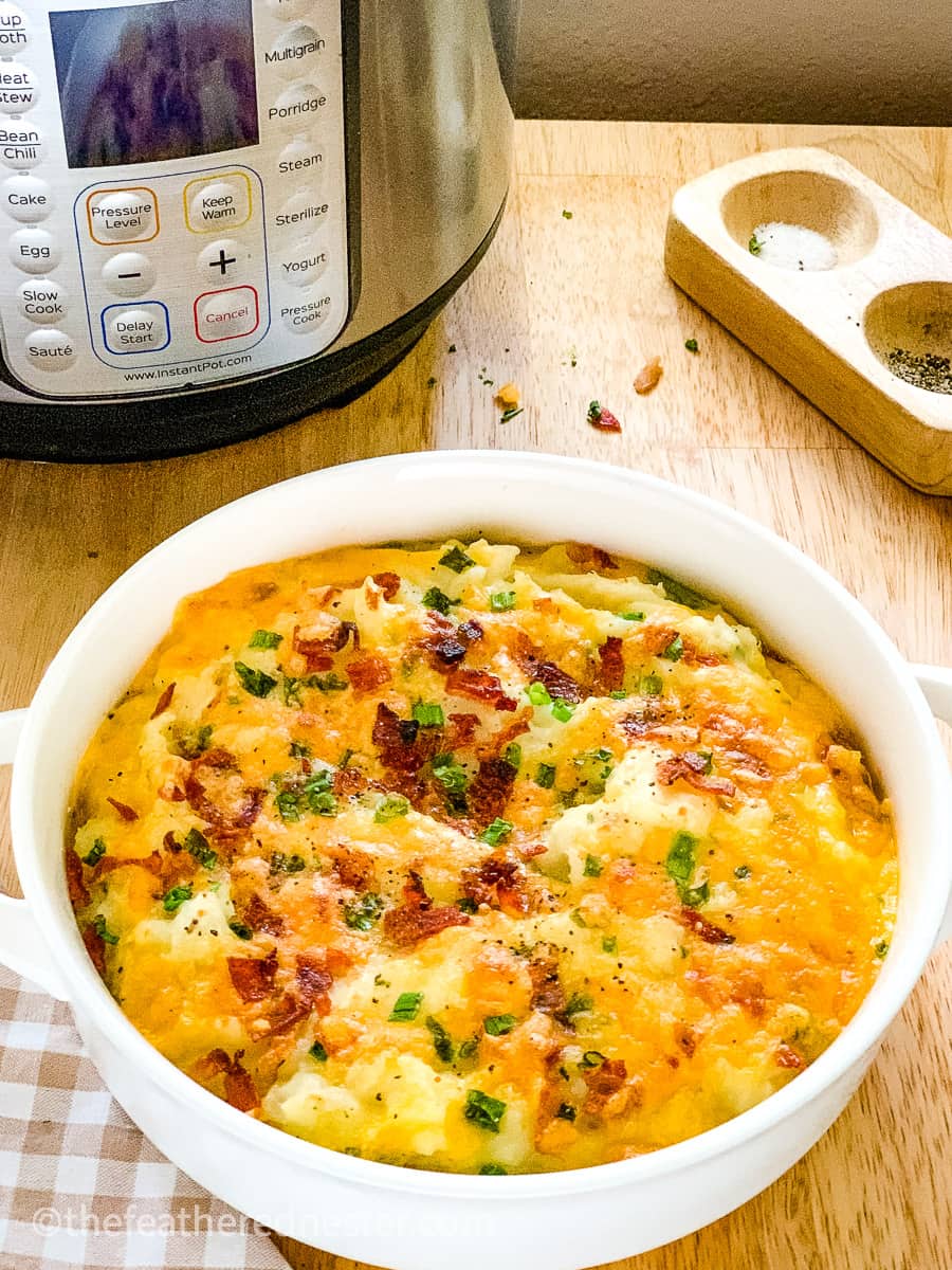 serving bowl of loaded potatoes with cheese, bacon bits, and green onion.