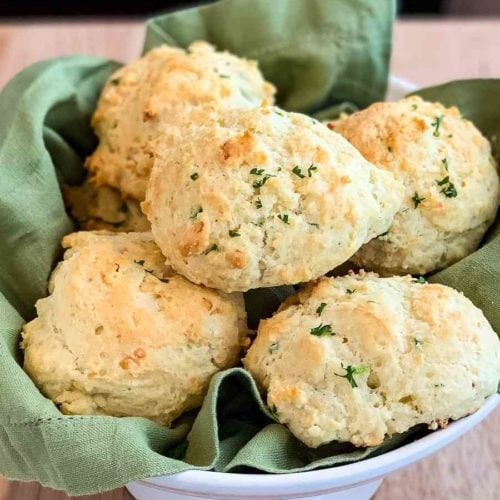 a basket of jalapeno cheddar biscuits in a white bowl lined with a green napkin.