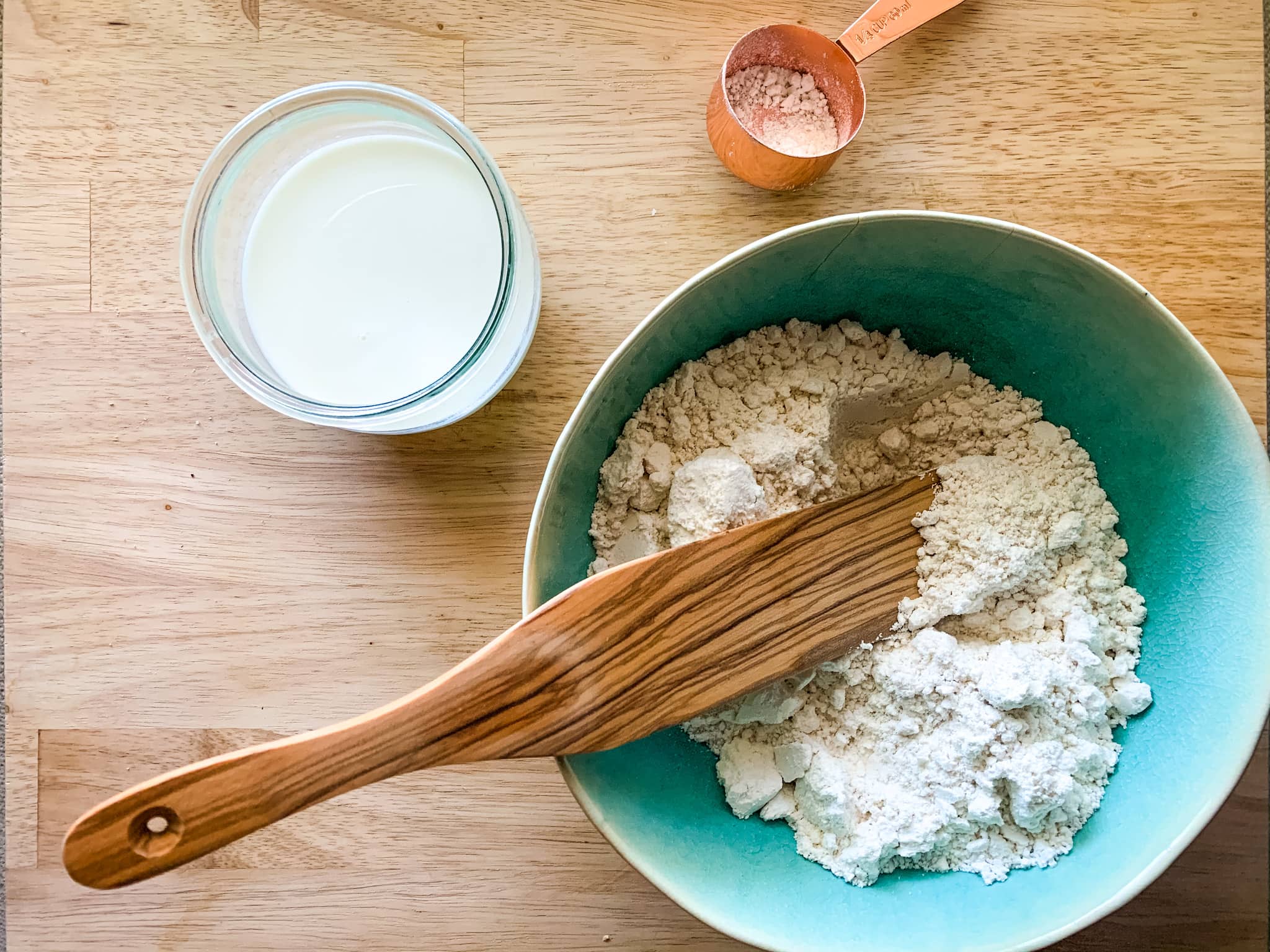 Bisquick biscuit mix in a green bowl with ladle and a glass of milk.