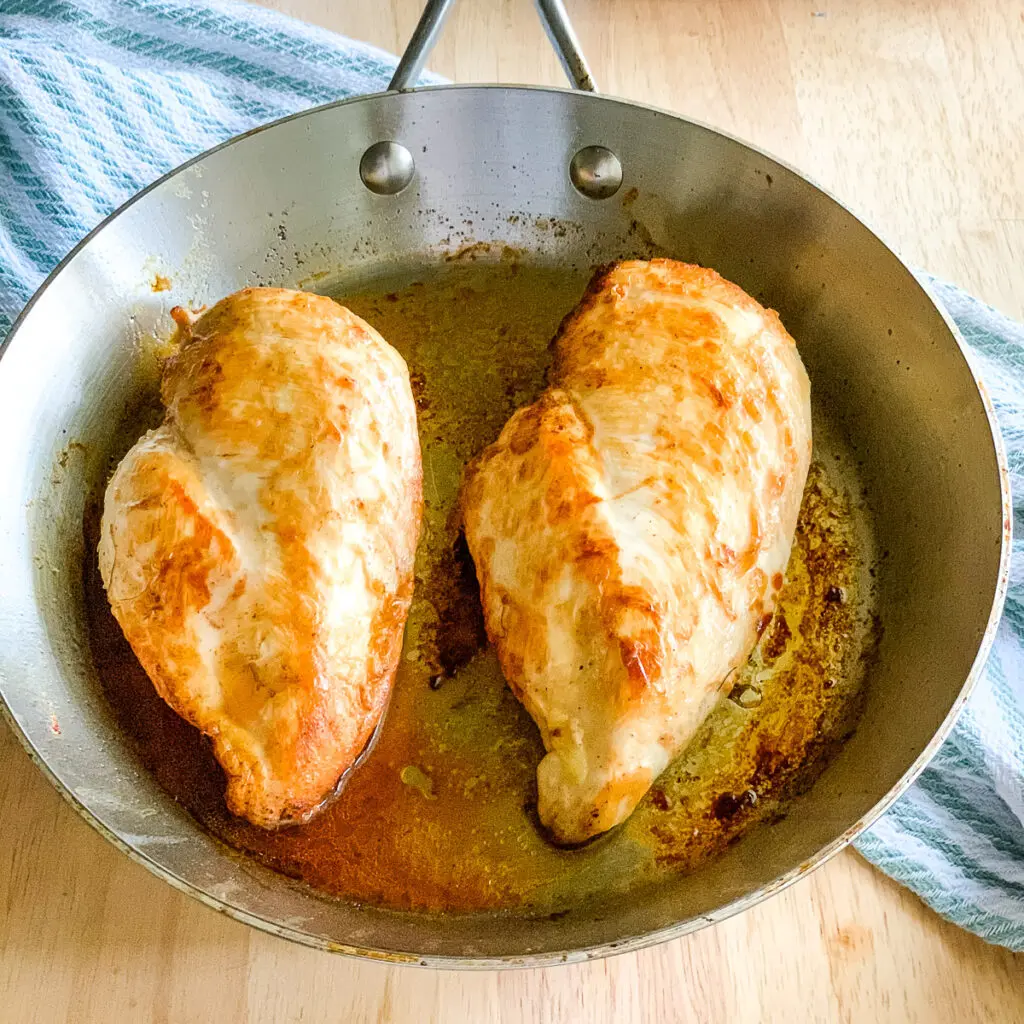 Two pan seared chicken breasts in a stainless skillet