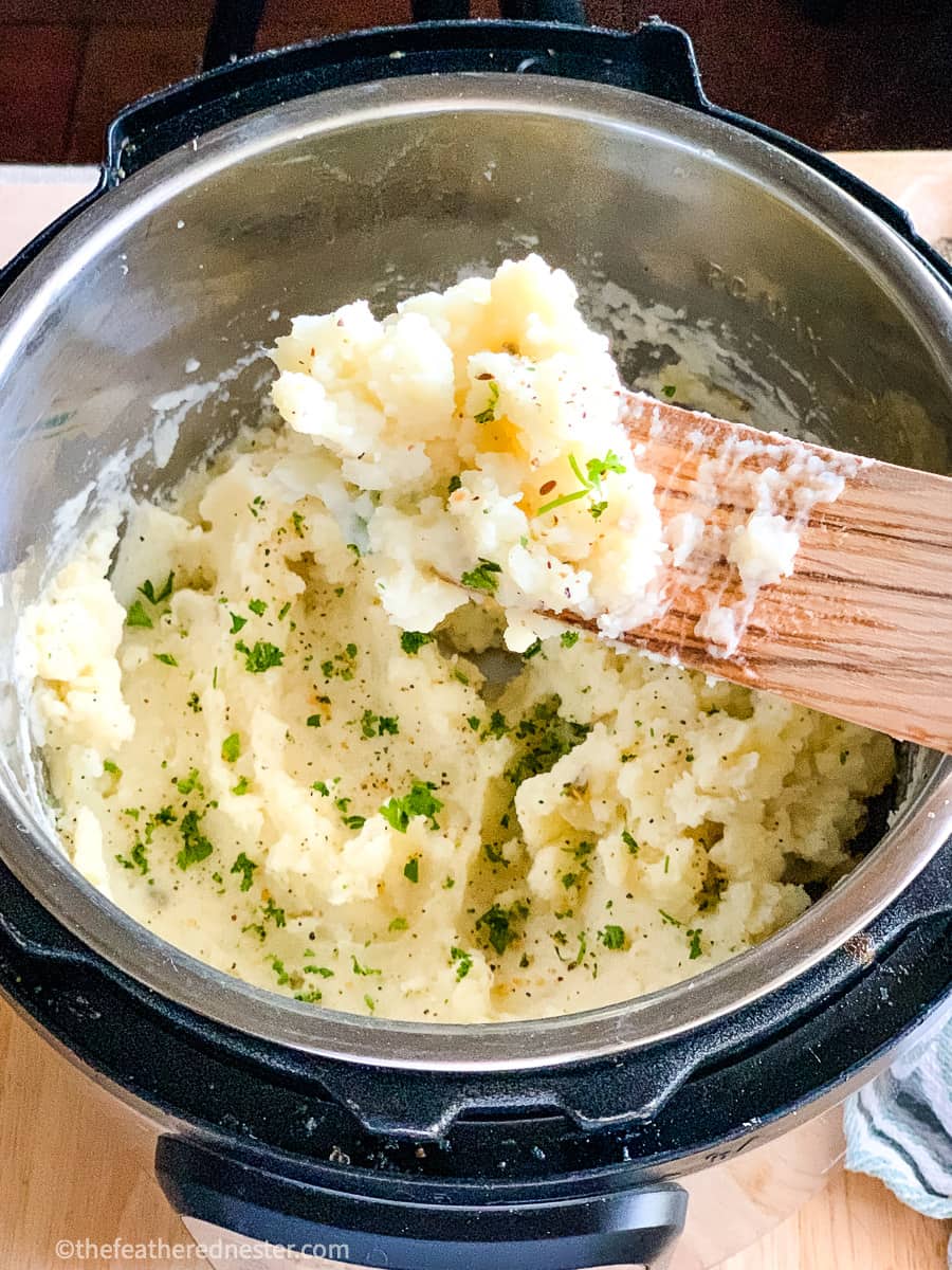 Close up of Instant Pot Mashed Potatoes on a wooden spoon held above the pressure cooker.