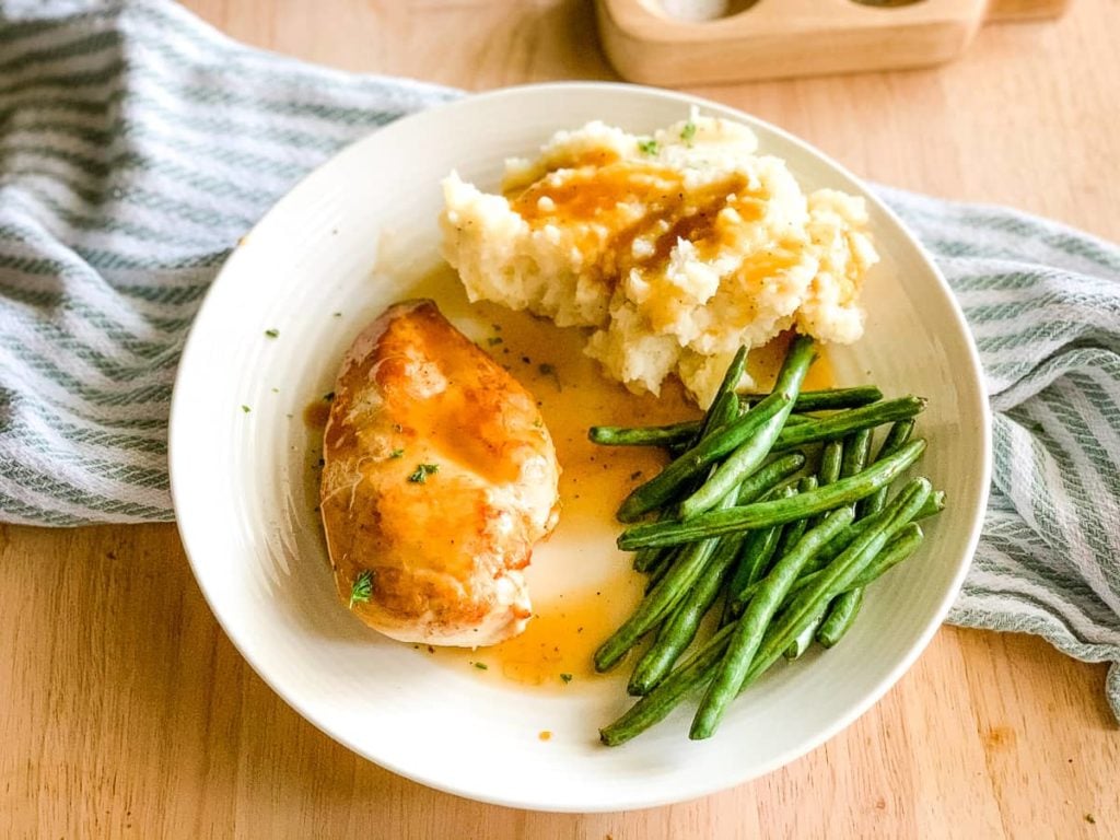 plate of mashed potatoes, green beans, and pan seared chicken with gravy