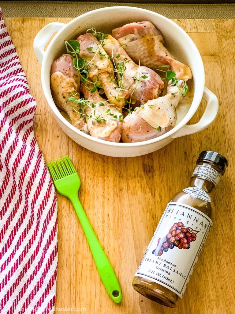 a bowl of chicken drumsticks with a bottle of balsamic dressing marinade