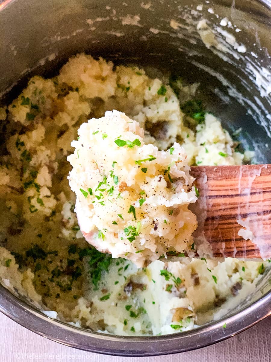 A wooden spoonful of mashed potatoes garnished with fresh parsley.