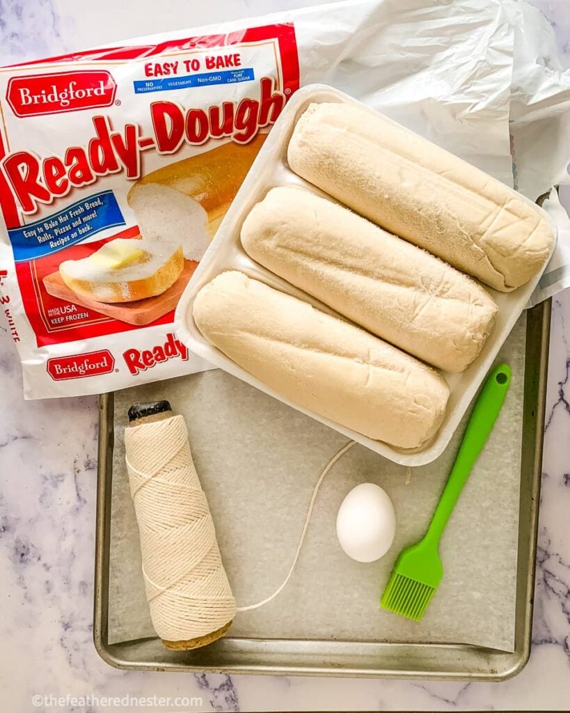 a tray of frozen bread dough loaves with an egg, pastry brush, twine, and a bag of Bridgford Ready-Dough