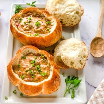 two bread bowls of cheeseburger soup on a white serving platter.