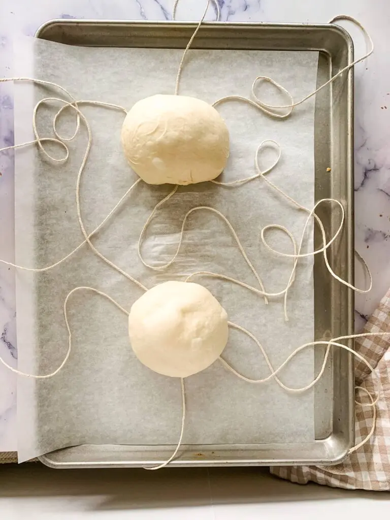 Sheet pan showing the frozen dough on top of the twine string for bread bowls
