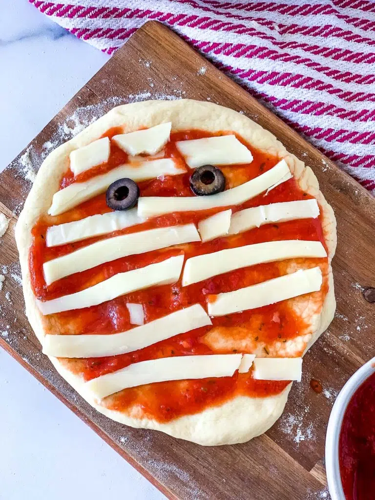a pizza with strips of mozzarella cheese to make it look like a mummy