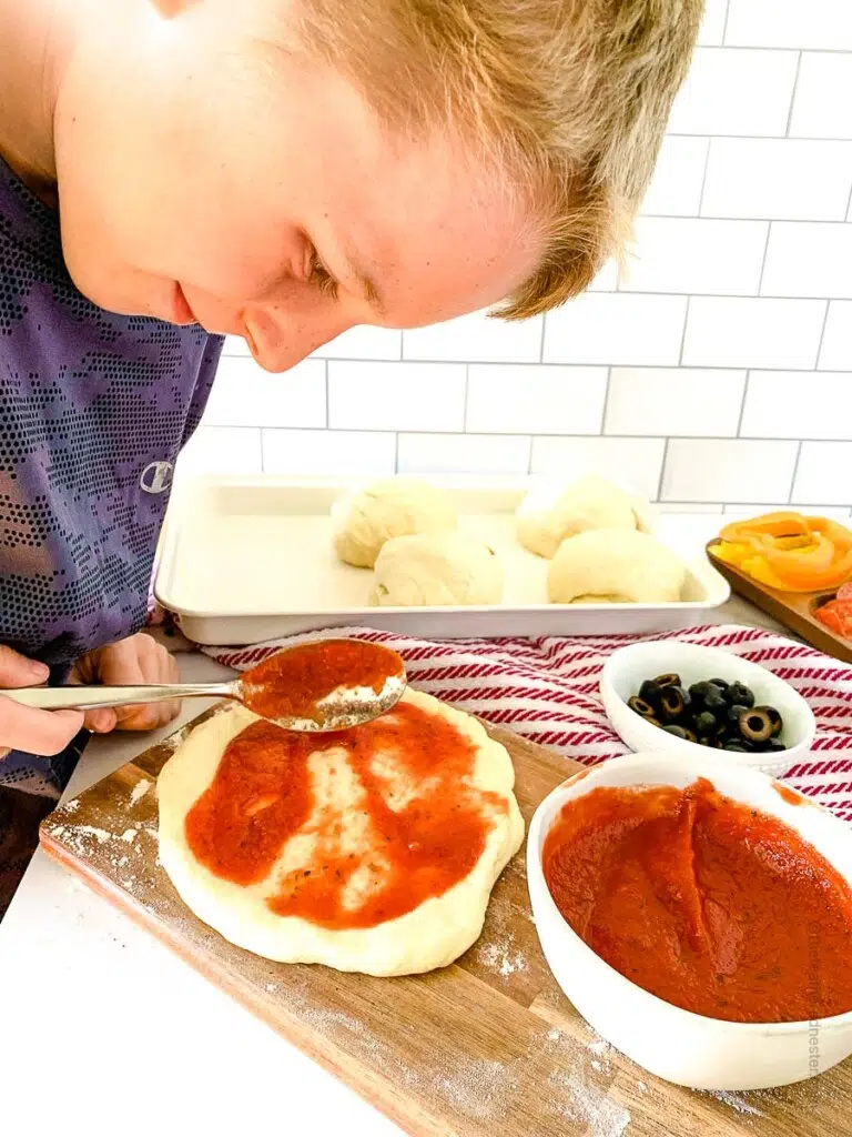 a boy spreading pizza sauce on pizza dough 
