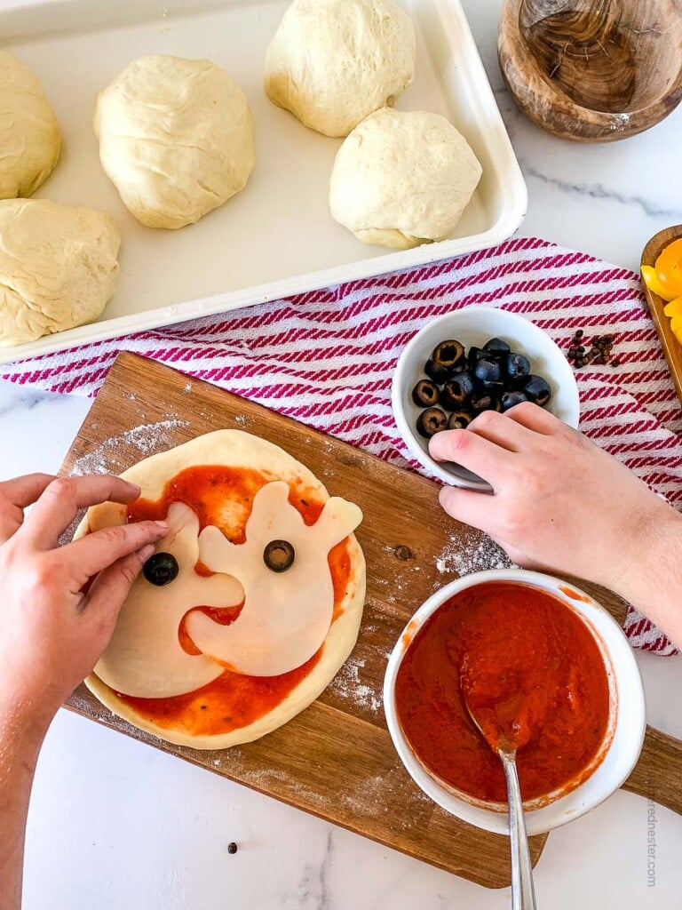 two hands putting together a ghost shaped pizza
