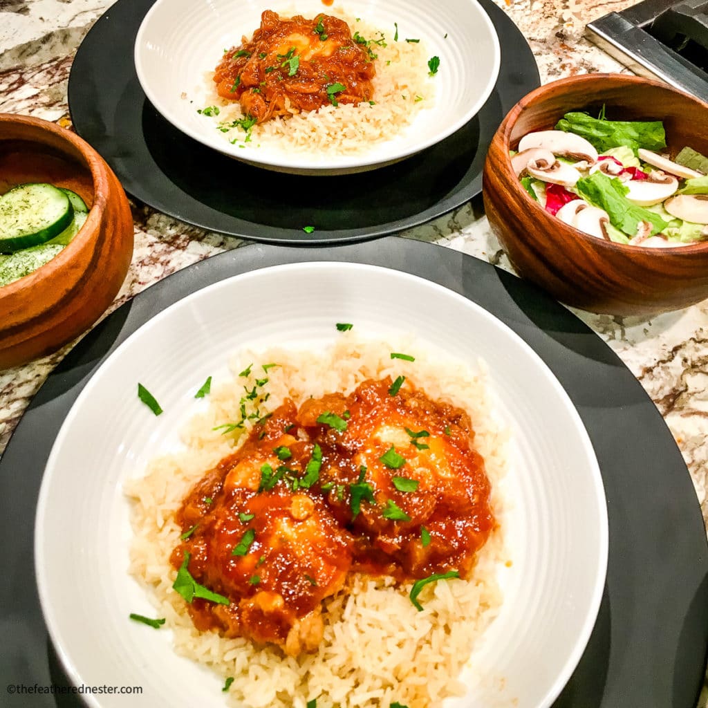 Two white plates with Huli Huli Chicken and two wooden bowls of vegetable sides.