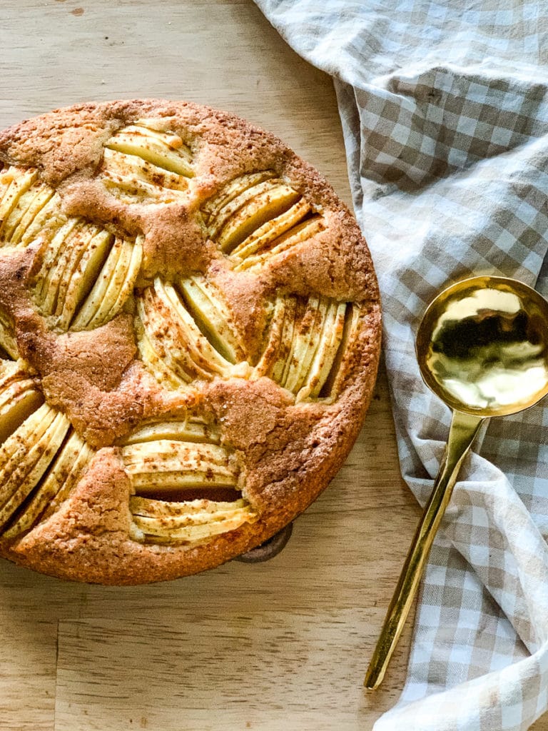 Apple kuchen on a table next to a gingham check linen kitchen towel and a gold serving spoon.