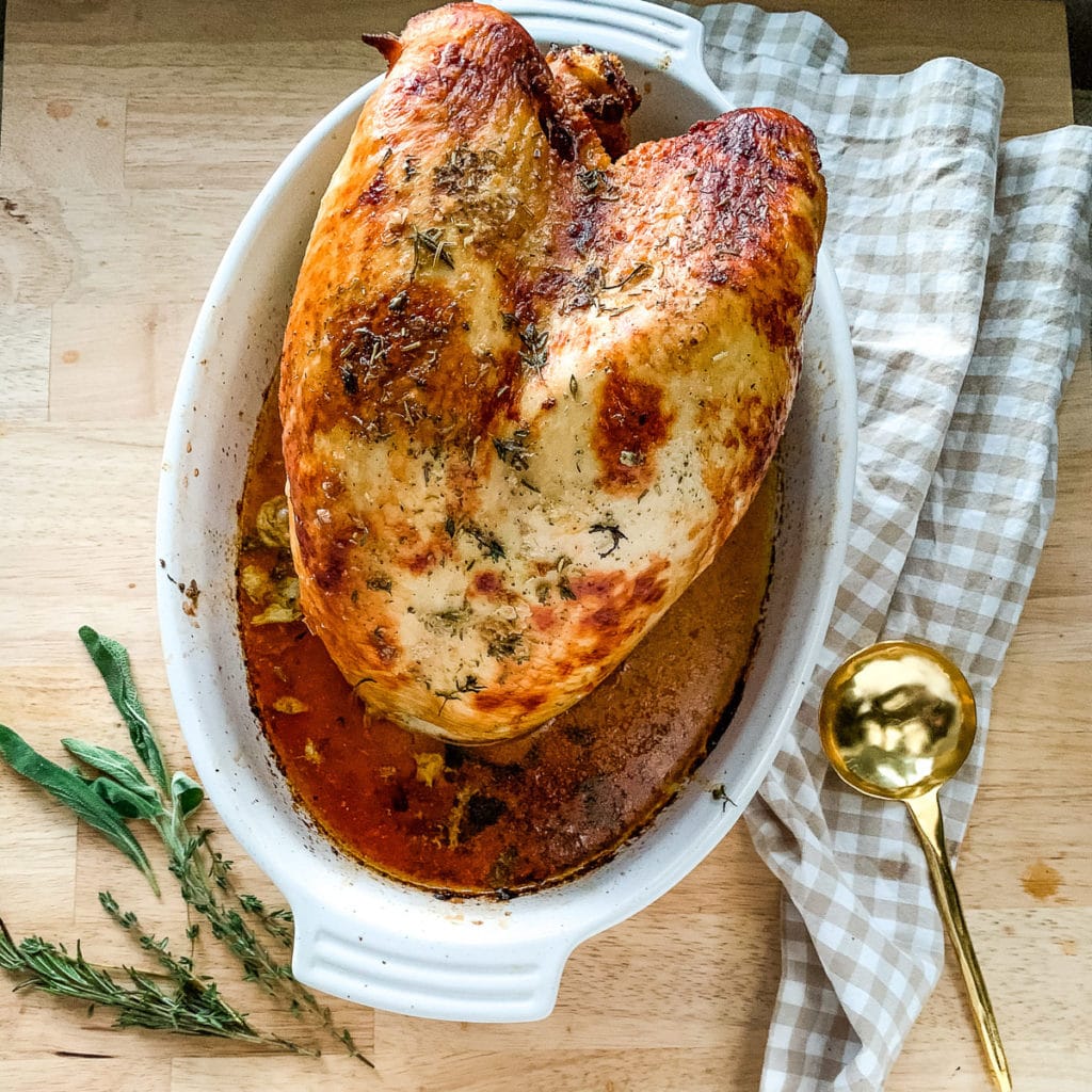 Fully roasted buttermilk brined turkey breast sitting in a roasting pan with its juices.