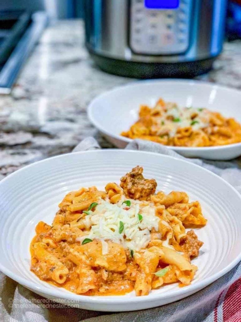 Two plated servings of lazy lasagna in front of an electric pressure cooker.