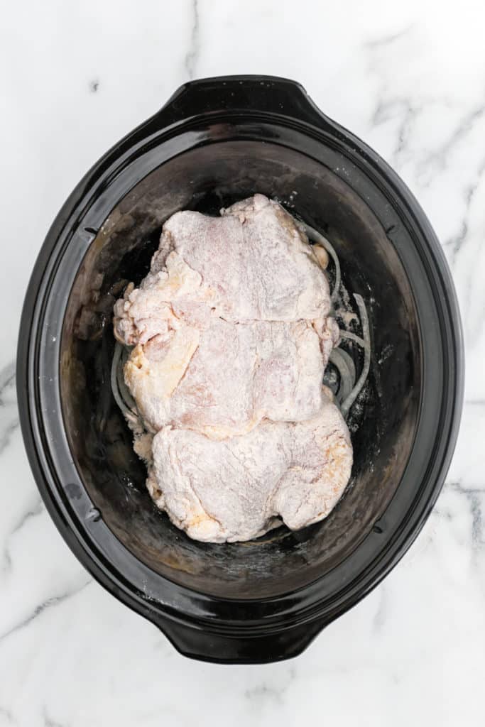 a crock pot with chicken thighs and sliced onions