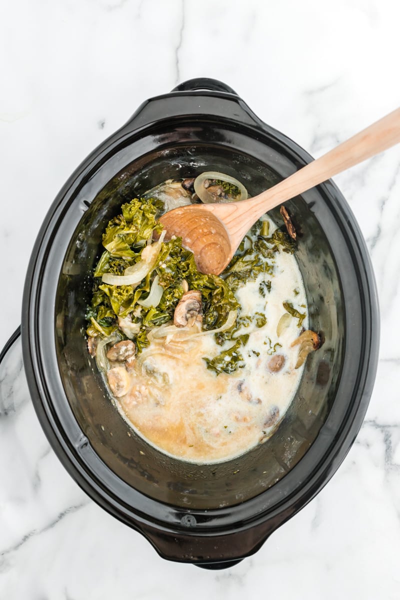 Chicken gravy and a wooden spoon with other ingredients in a crockpot.