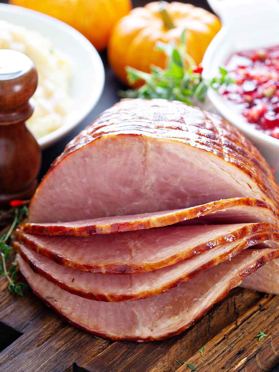 Ham slices on a serving board with side dishes around it.