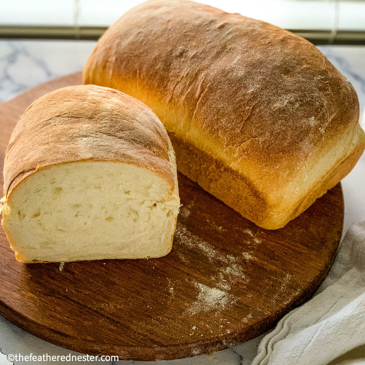 two loaves of sourdough sandwich bread on a wooden cutting board.