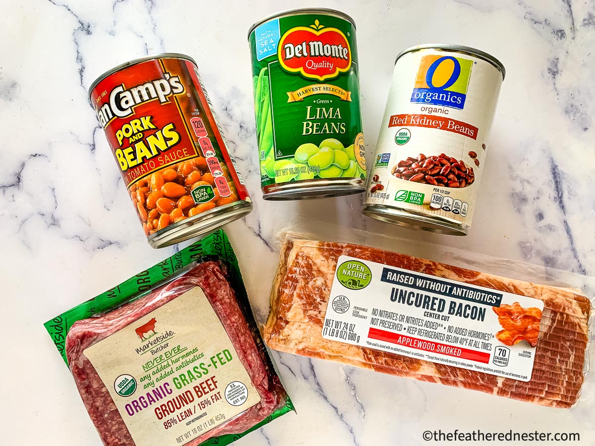 More ingredients for this beans recipe: a can of pork and beans, a can of lima beans, a can of red kidney beans, a package of uncured bacon, and a package of ground grass-fed beef.