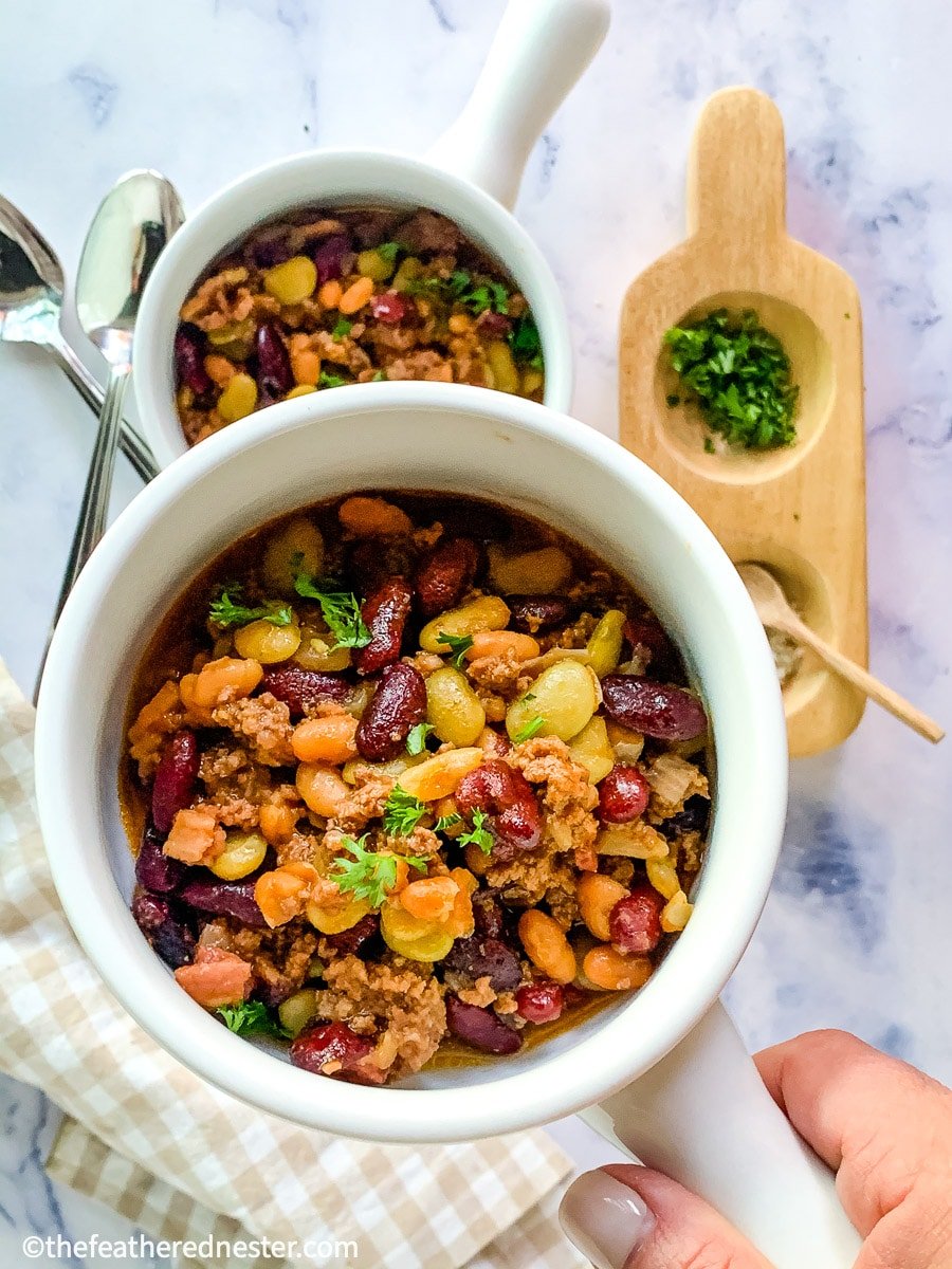 Instant Pot calico beans close up with another in the background as well as a tan checked napkin and a wooden bowl of spices.