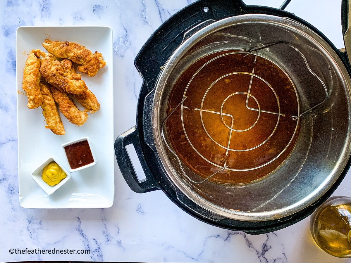 Cooked tenders on a platter with dipping sauces next to an Instant Pot pressure cooker with trivet inside.