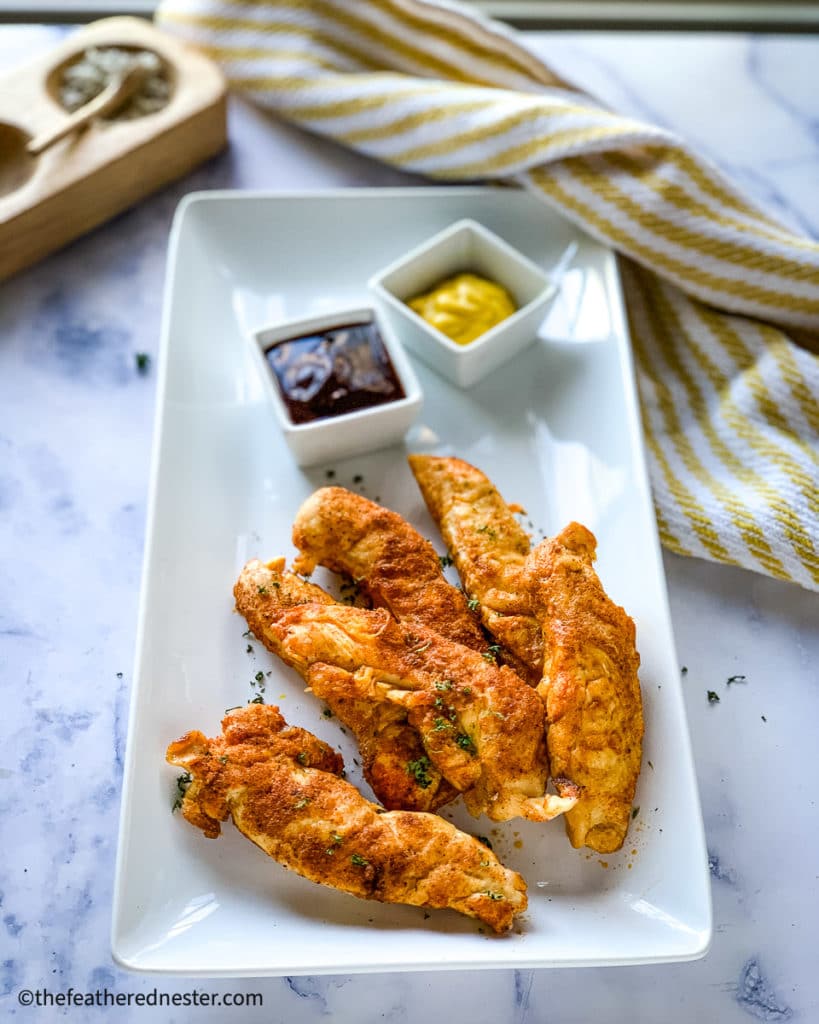 a platter of Instant Pot chicken tenders with mustard and BBQ dipping sauces.