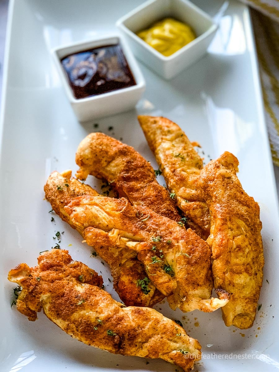 a plate of Instant Pot Chicken Tenders with honey mustard and barbecue dipping sauces.