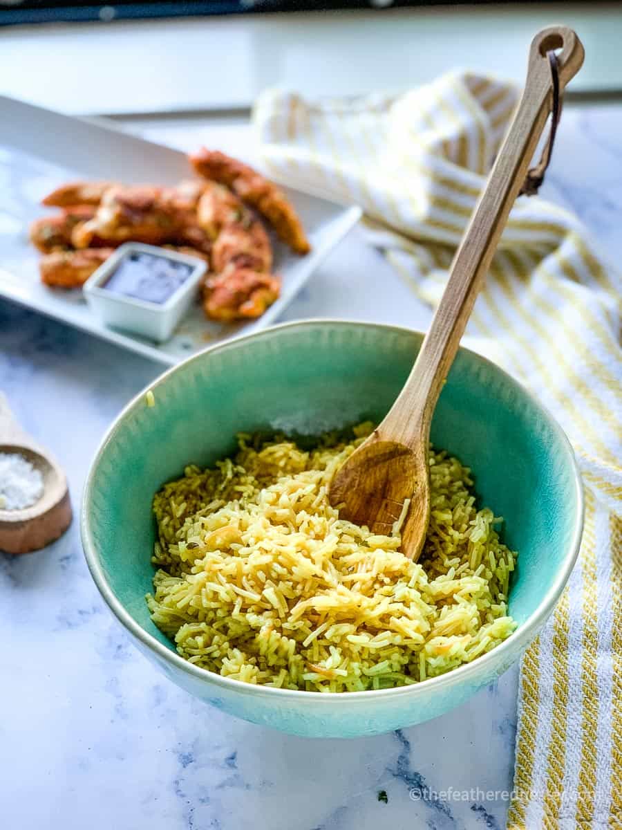 Rice A Roni in a green bowl with a platter of chicken in the background.