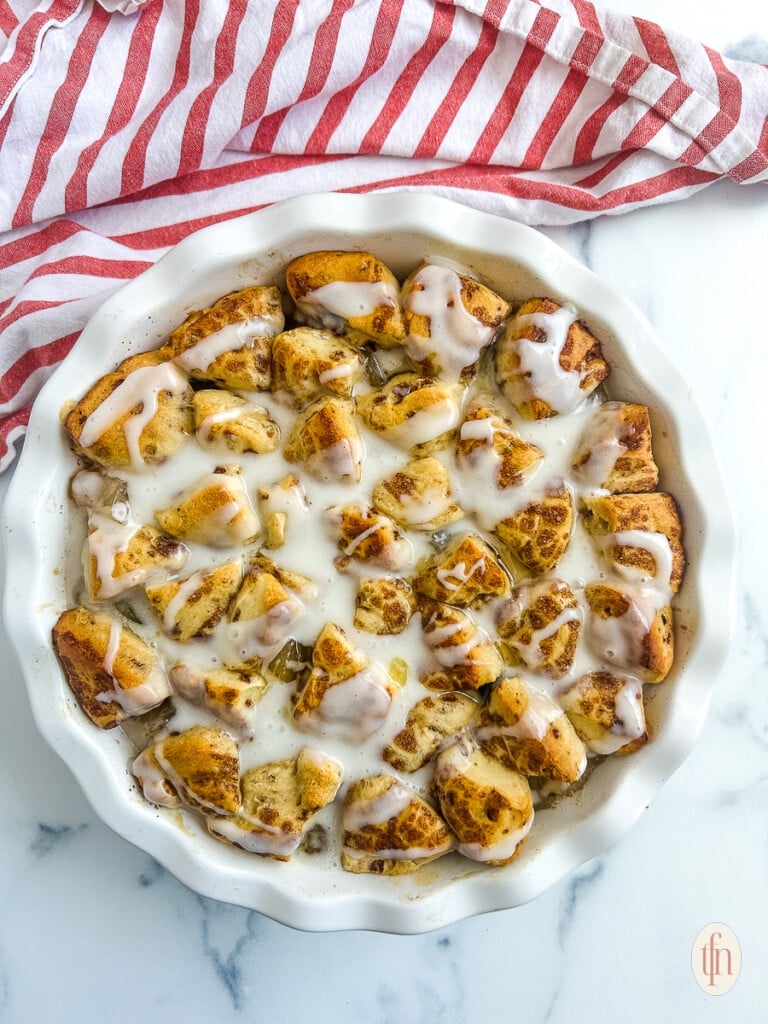 Cinnamon rolls with apple pie filling in a white dish on a white marble background.