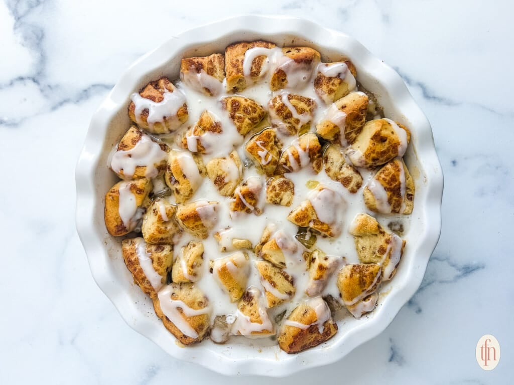 Cinnamon rolls with apple pie filling in a white dish on a white marble background.