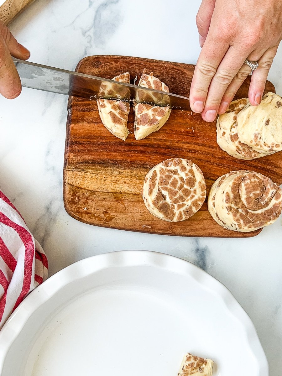 Cutting cinnamon roll rounds into fourths with a knife on a cutting board.