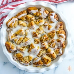 Cinnamon rolls with apple pie filling in a white dish on a white marble background.