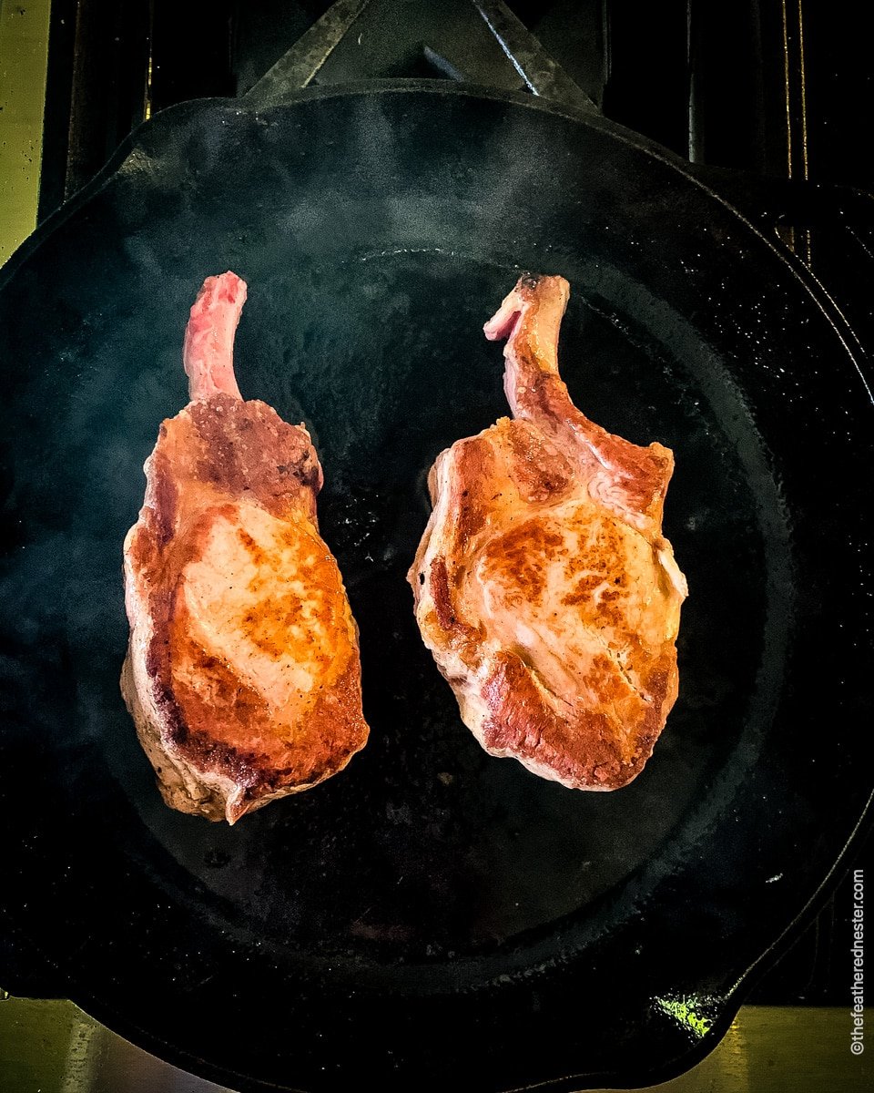 Searing two tenderized pork chops in a cast iron skillet.