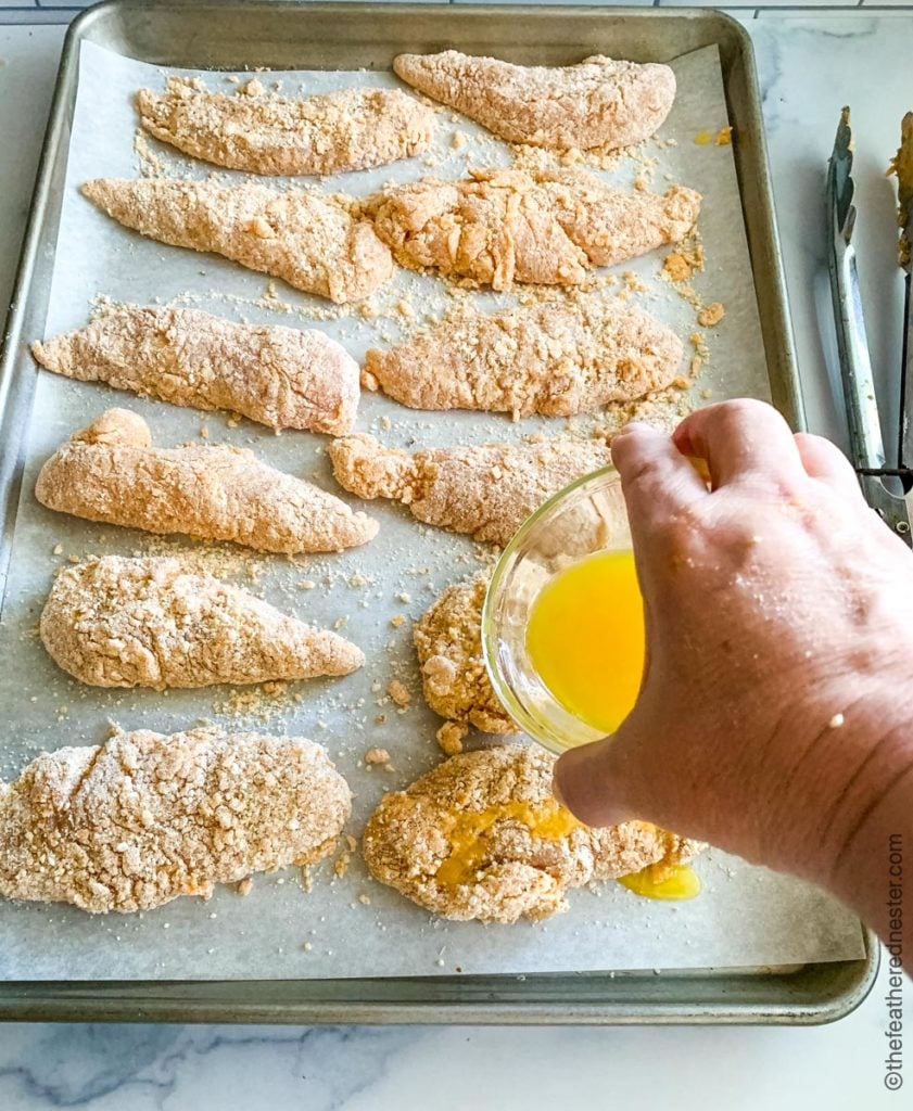 drizzling melted butter over bisquick chicken tenders on a baking tray