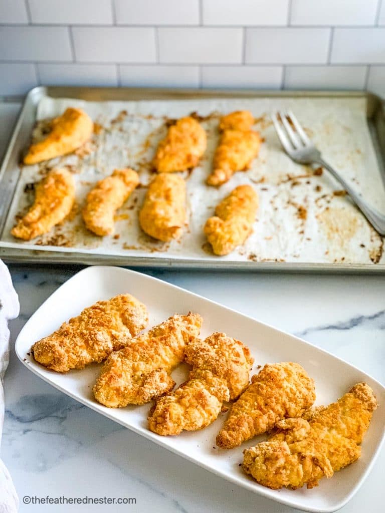 a platter of bisquick chicken tenders with a baking sheet of them in the background.