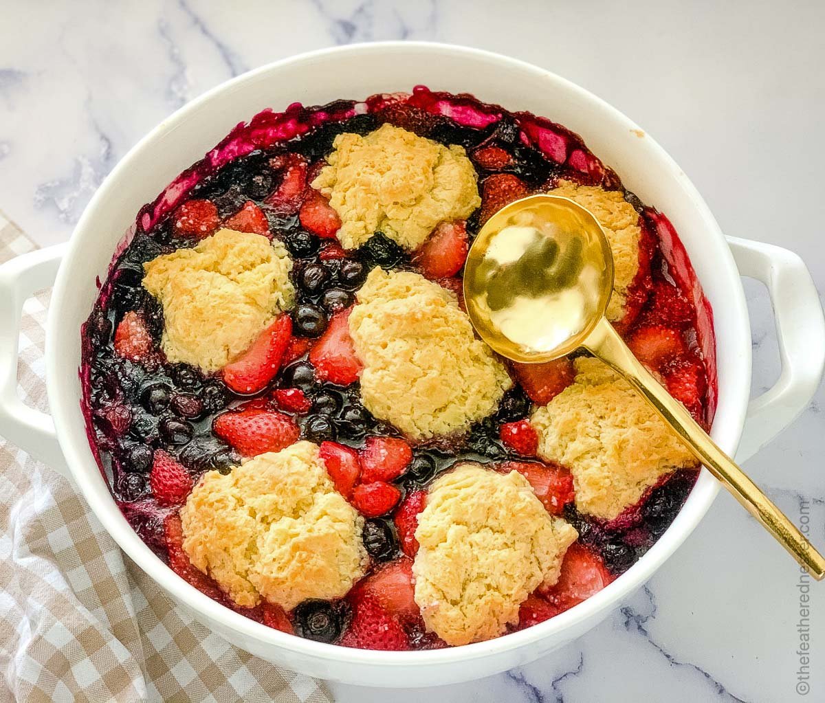 Strawberry blueberry cobbler on a white dish with spoon. 